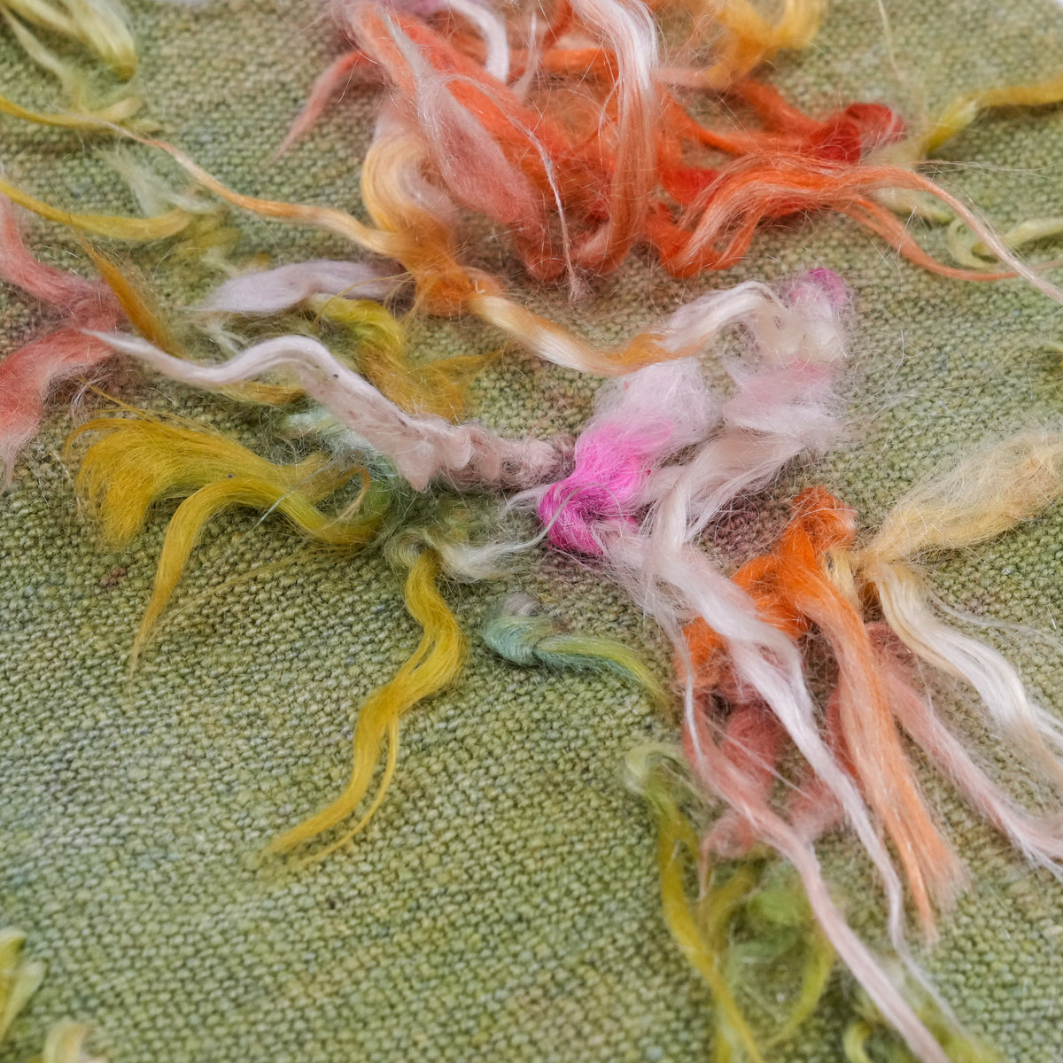 Green scattered-motif cushion covers — detail of orange, pink and yellow tassel tufts dotted over the ground