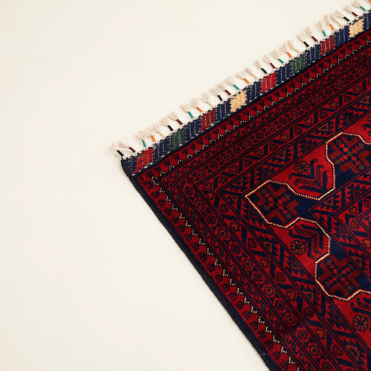 Bordo geometrik desenli halı — köşe yakın planı, renkli sarımlı saçak ucu
