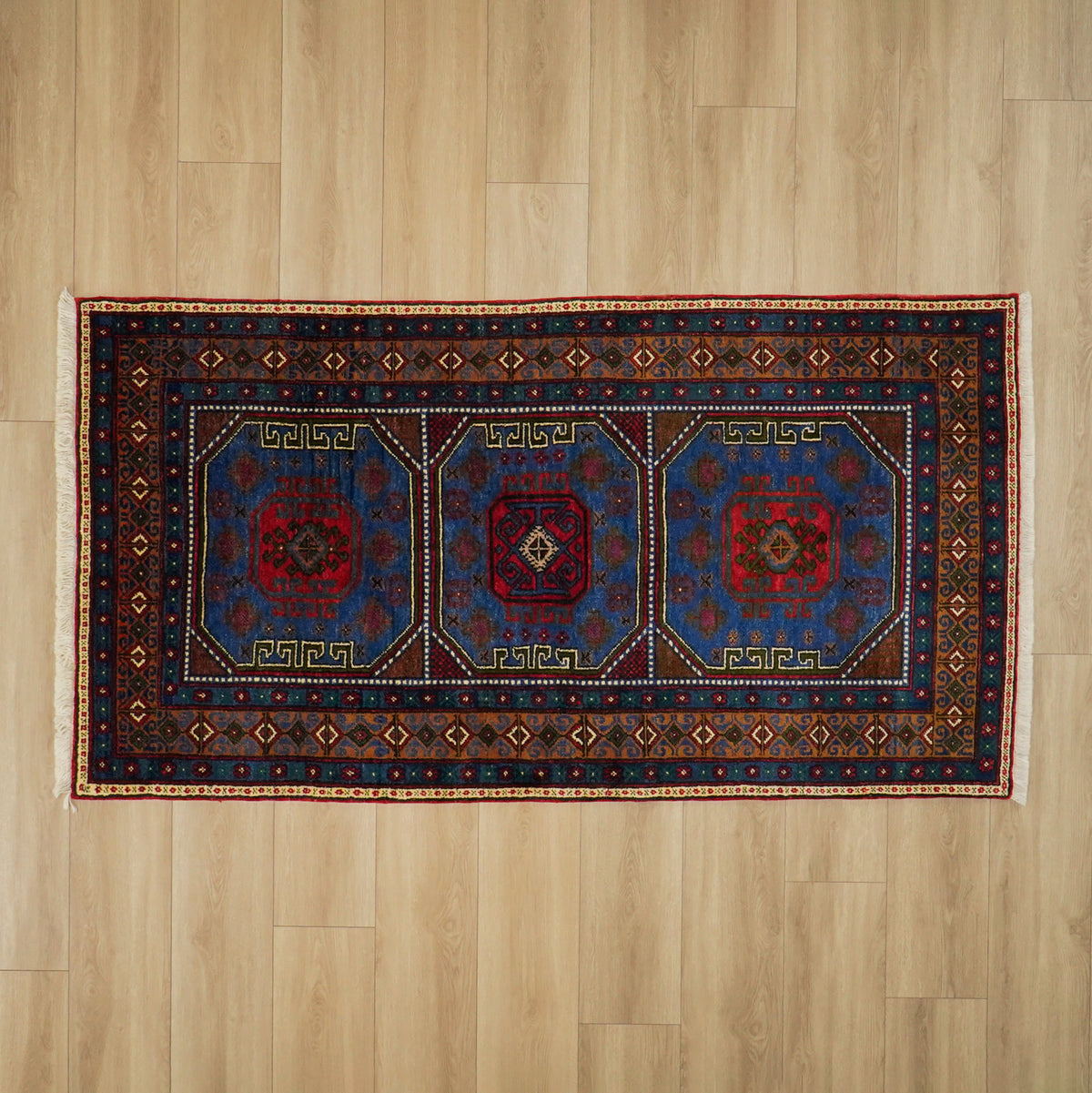 Navy ethnic-pattern rug — the whole piece from overhead on light parquet, floor space around it