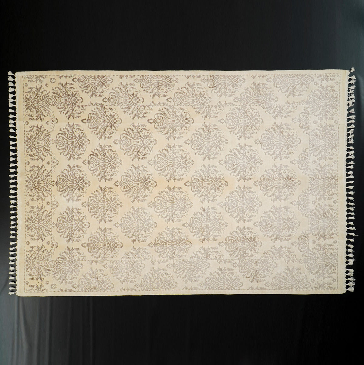 Krem damask desenli halı — siyah fonda cepheden tam boy, iki uzun kenarda püskül dizisi