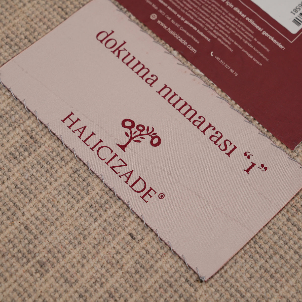 Günyolu Series amber-half-disc gray abstract rug — a pink ribbon label and a burgundy card on the beige backing