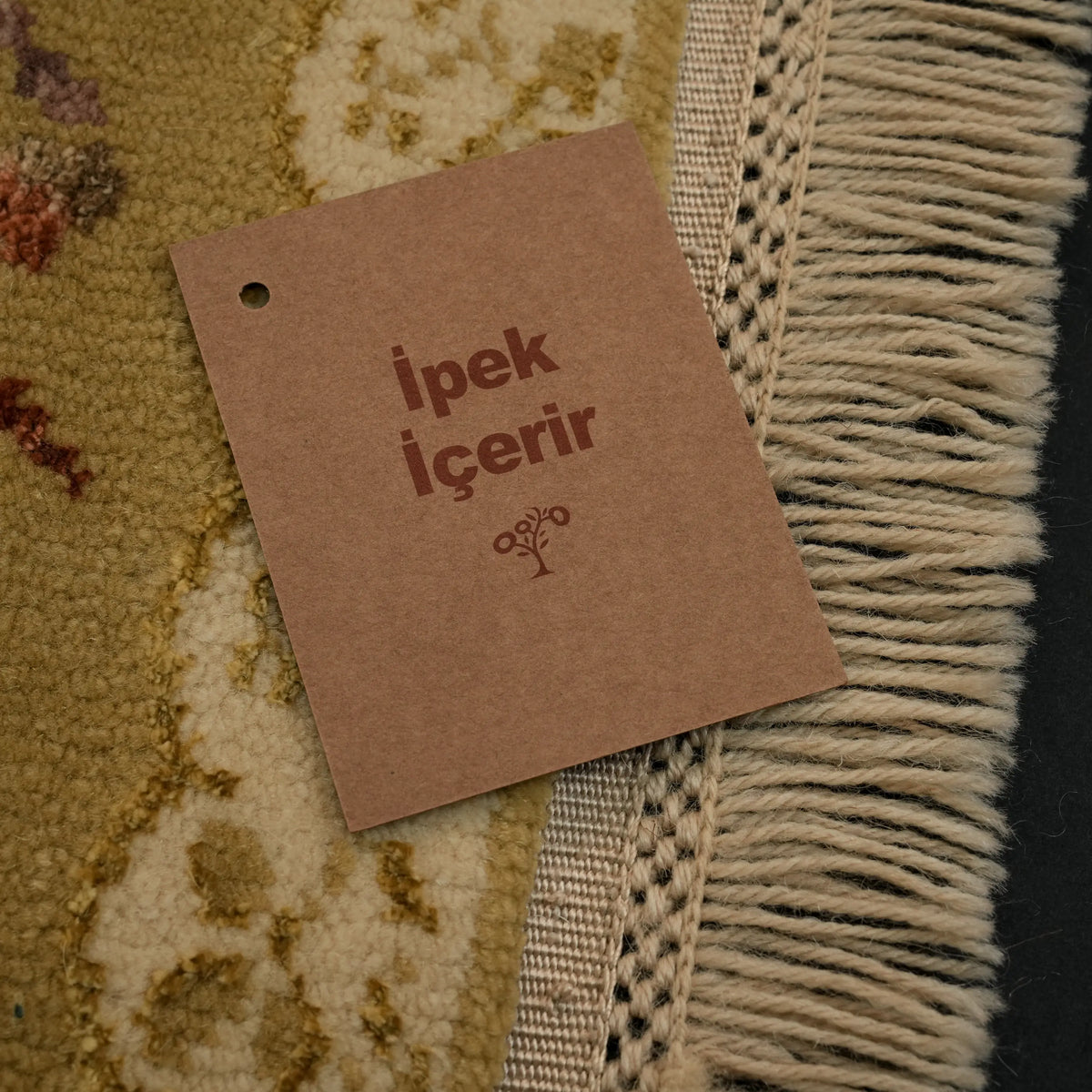 Harem Series mustard-border beige Oushak-pattern rug — the flat stripe at the base of the fringe and a kraft tag on the pile