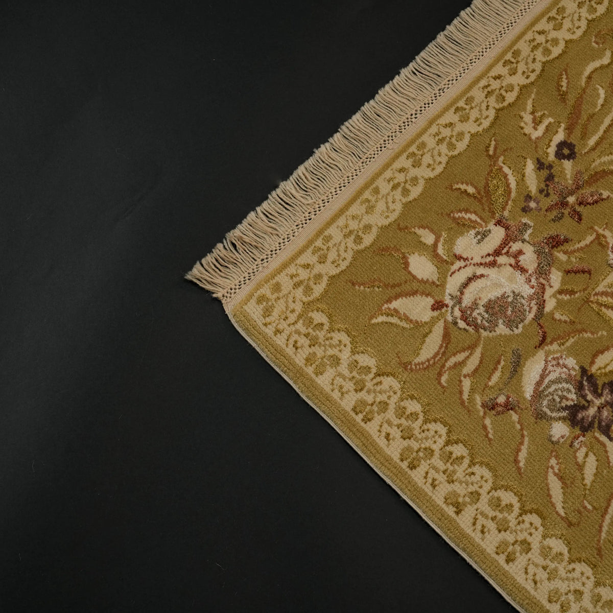 Harem Series mustard-border beige Oushak-pattern rug — the end framed on a black backdrop; the row of fringe and a large flower spray above it