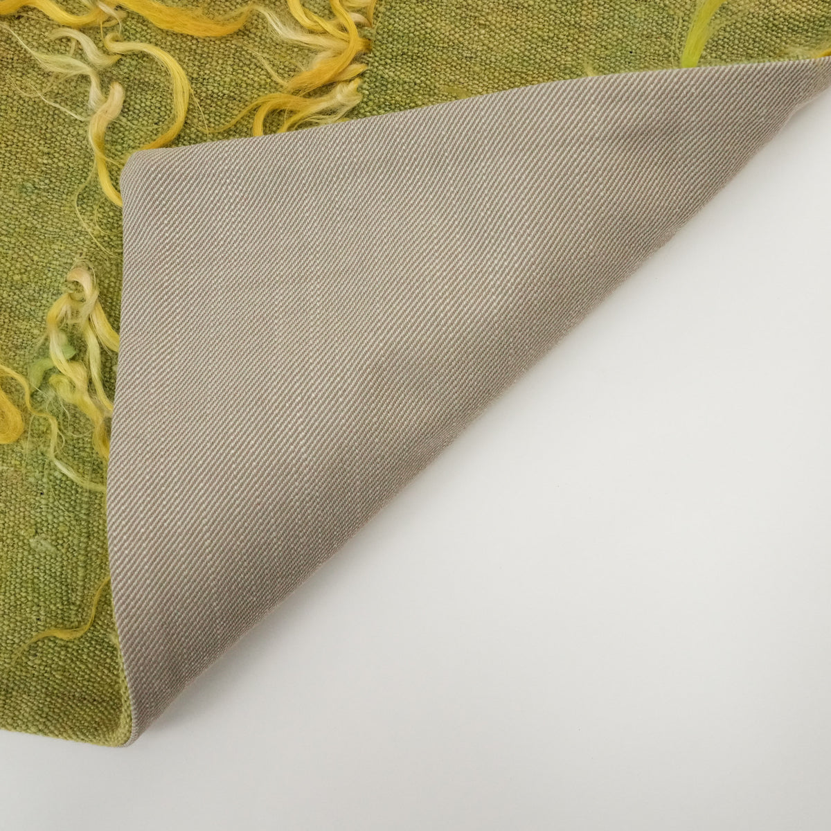 plain green cushion cover — corner opened on a white background, beige backing fabric beside the green front