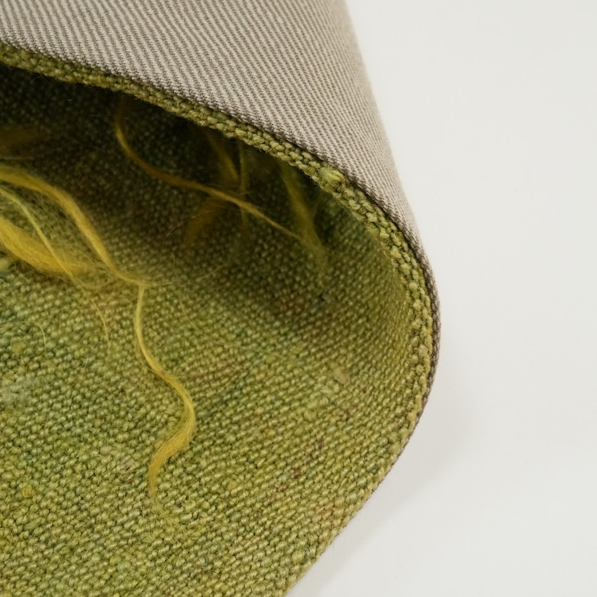 plain green cushion cover — green surface along the curling edge, yellow yarn ends