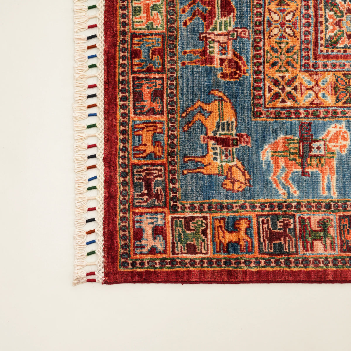 Şahzade Series blue-and-red patterned rug — corner close-up, horse figures on the blue border and a colored tassel