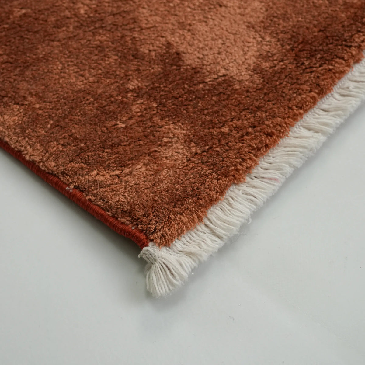 Velvet terracotta plain rug — the corner up close, a tuft of cream fringe and the curling edge