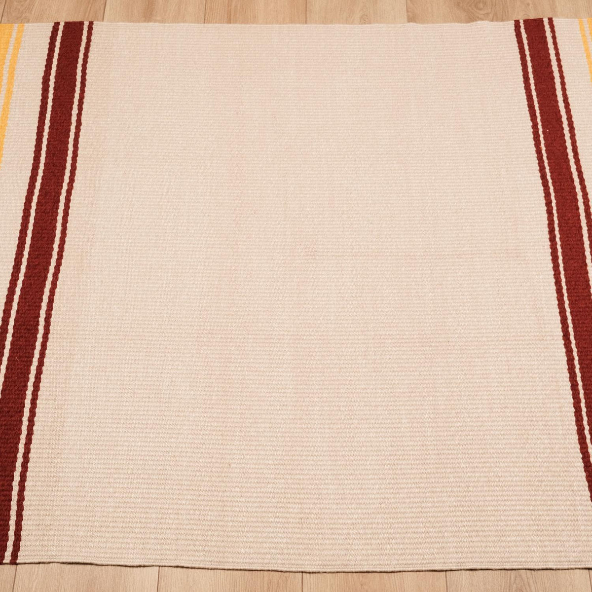 cream striped kilim — head-on on a wood floor, burgundy stripe bands along both sides