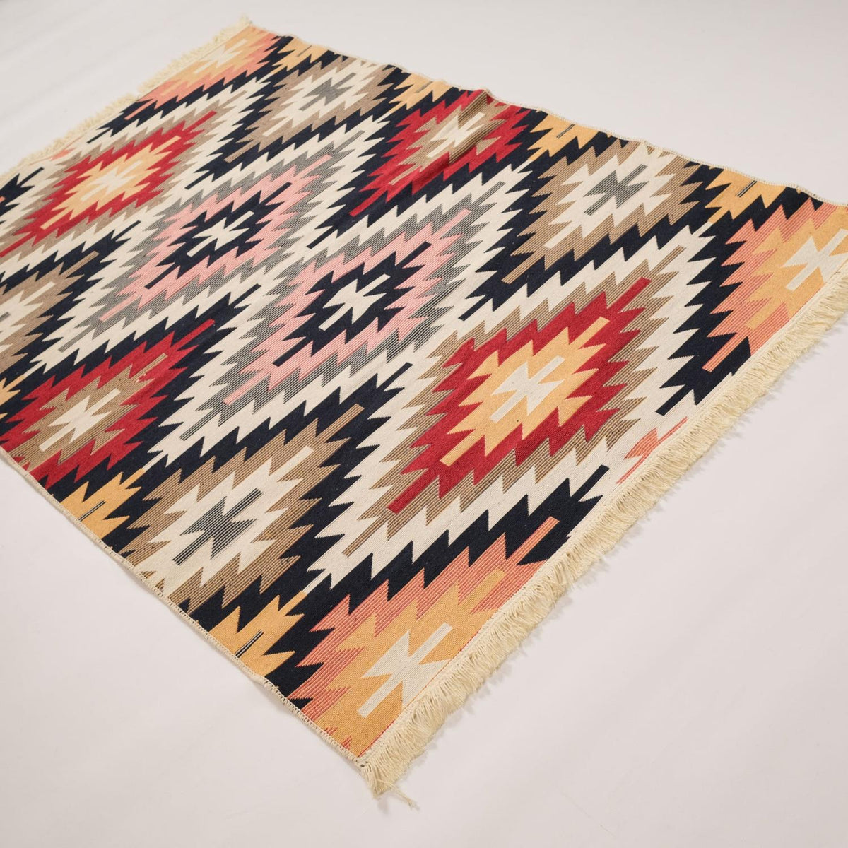 Kehribar Series multicolor Anatolian-pattern kilim — salmon and beige corner on a light backdrop; short cream fringe