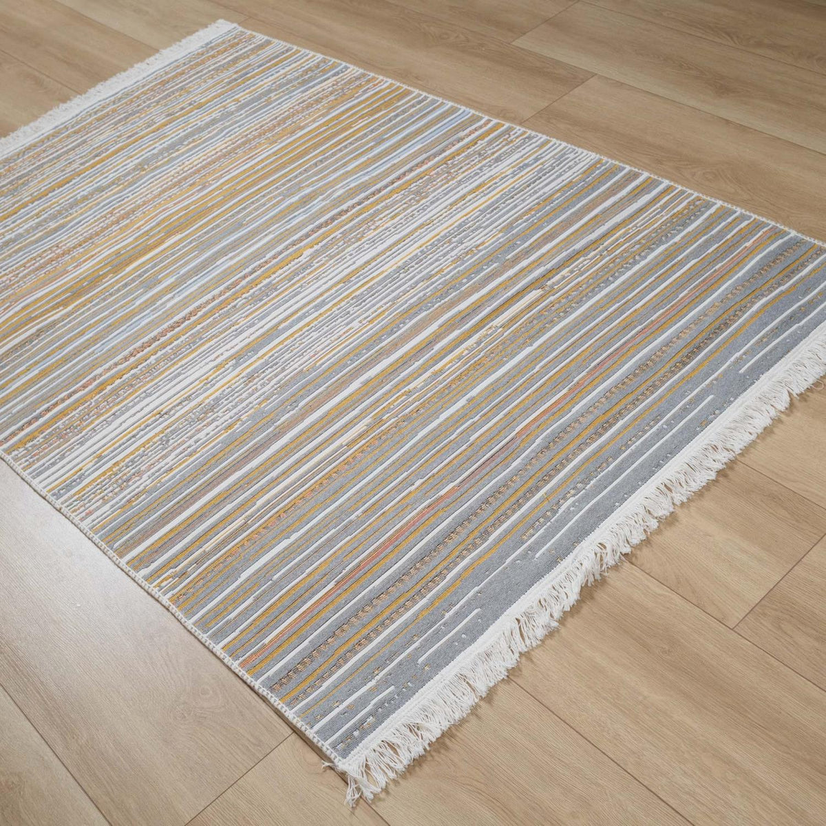 Kehribar Series multicolor striped kilim — angled full length on parquet, thin mostly gray bands, fringe at the corner