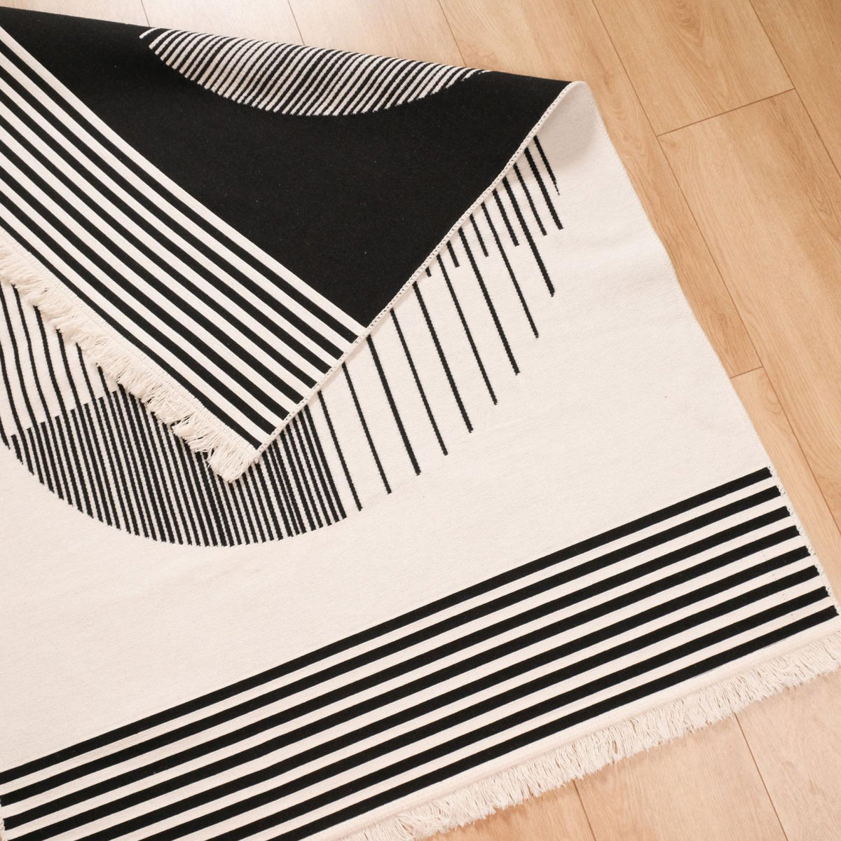 Kehribar Series black striped kilim — corner folded, the black side emerging from under the cream face