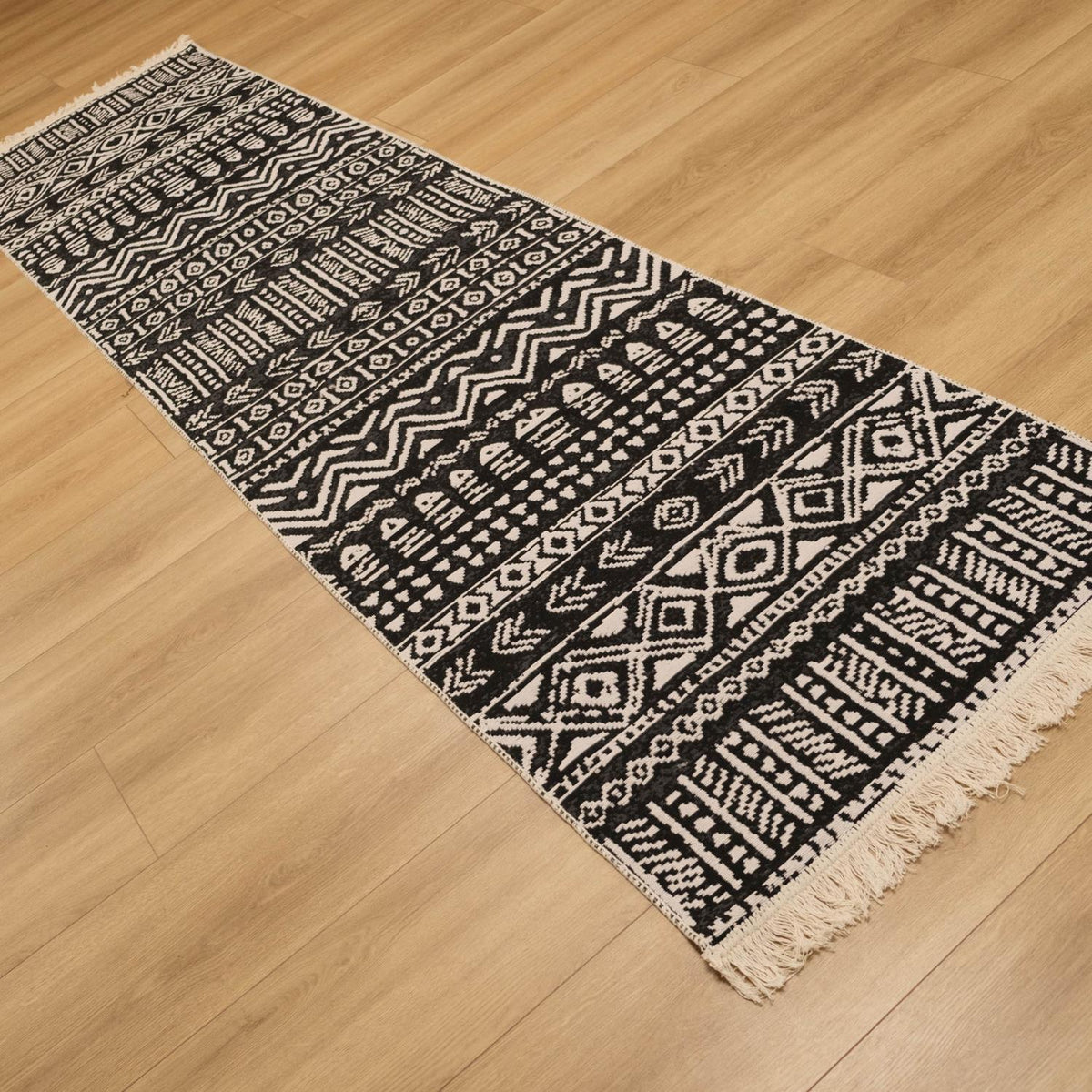 Kehribar Serisi siyah geometrik desenli kilim — koyu yüzlü yolluk kareyi çaprazlıyor, sağ altta saçak