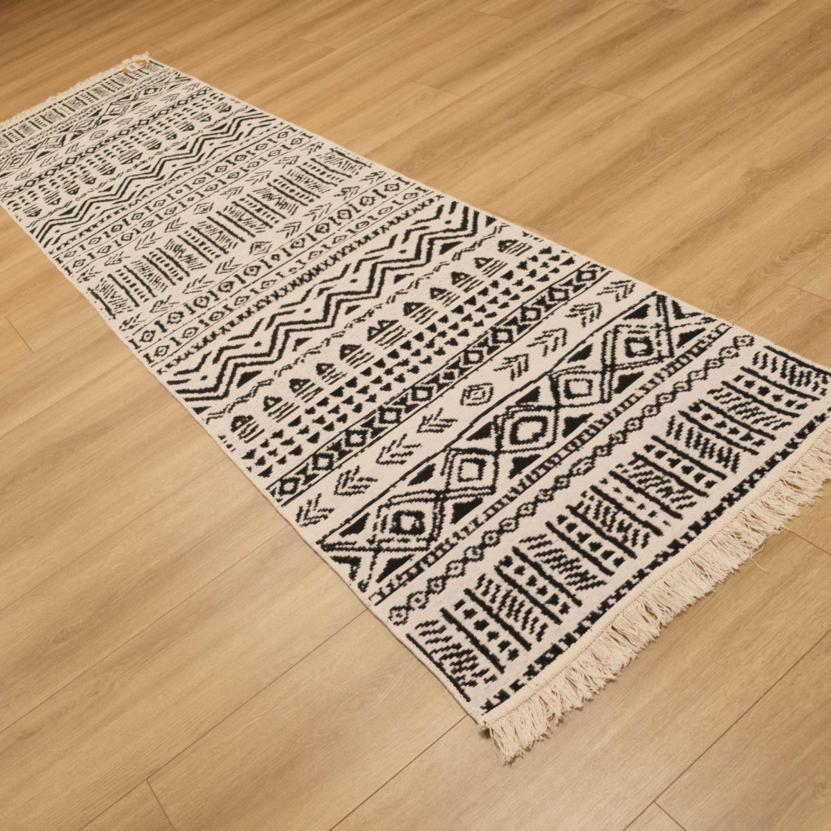 Kehribar Serisi siyah geometrik desenli kilim — krem yüzü üstte, parkede çapraz uzanıyor