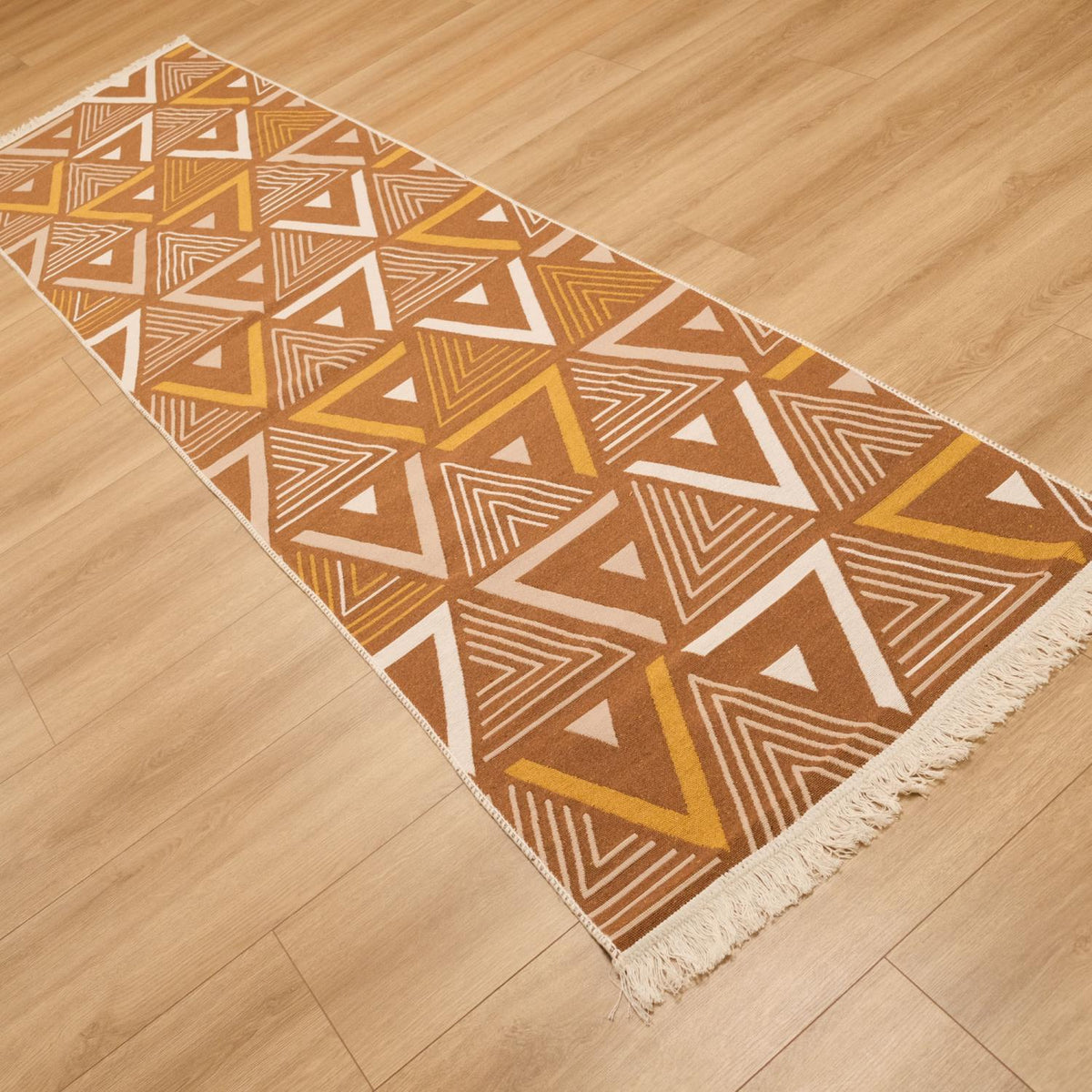 Kehribar kahverengi üçgen desenli kilim — ahşap zeminde kahverengi yüzü üstte, açılı serili